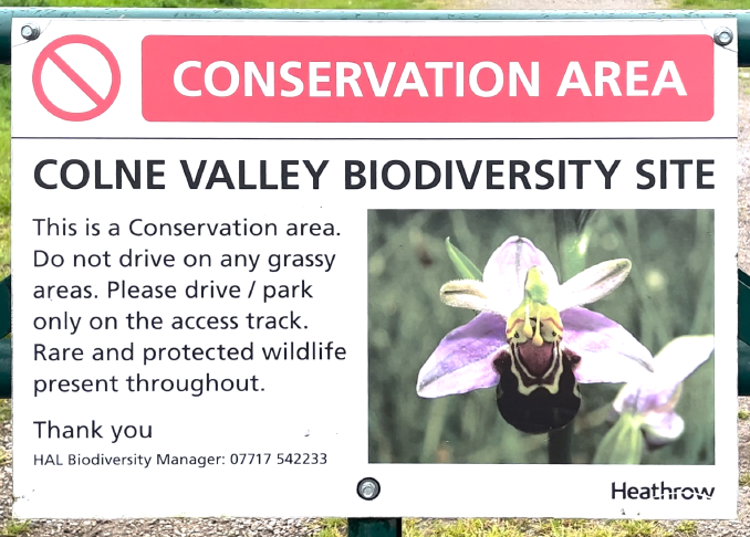 A white sign with a red prohibition symbol top left and the header &lsquo;CONSERVATION AREA&rsquo;. &lsquo;Colne Valley Biodiversity Site. This is a Conservation area. Do not drive on any grassy areas. Please drive / park only on the access track. Rare and protected wildlife present throughout. Thank you.&rsquo; This is followed by a picture of a flower