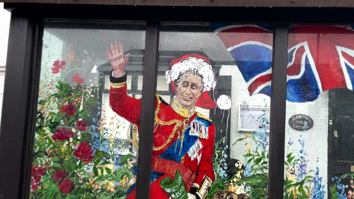 King Charles painted on a bus stop with a santa hat badly painted on his head