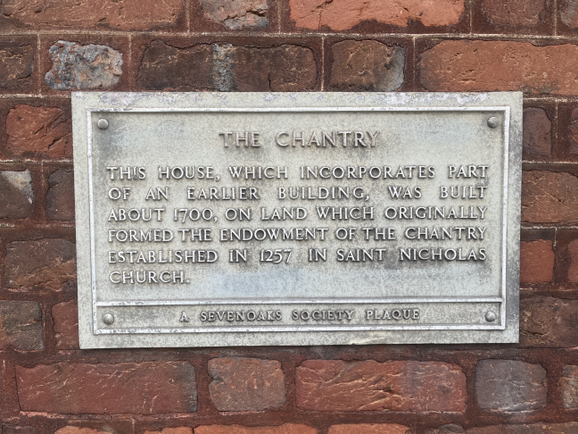 A grey plaque on a wall reading: The Chantry. This house, which incorporates part of an earlier building, was built about 1700, on land which originally formed the endowment of the chantry established in 1257 in Saint Nicholas Church.